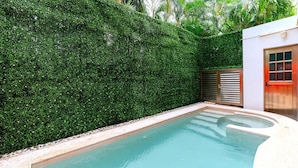 A swimming pool with a surrounding hedge, a door with a red frame, and a small building with a window. - Beach Apartment#3 2BDR 1BTH in Villas Playa Blanca (Cancún)