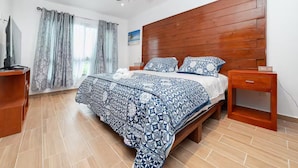 A bedroom with a wooden headboard, a bed with a blue and white patterned bedspread, a wooden nightstand, and a ceiling fan. - Beach Apartment#3 2BDR 1BTH in Villas Playa Blanca (Cancún)