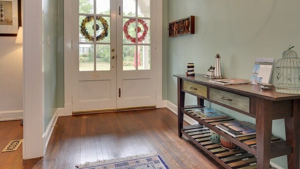Un couloir doté d’un plancher en bois, une porte avec deux panneaux de verre et une petite table sur laquelle sont posés des livres et des objets décoratifs.