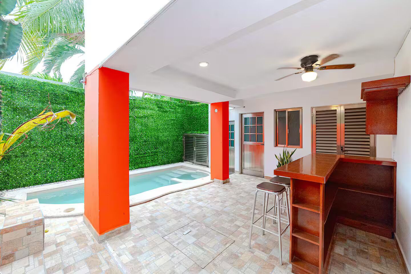 A covered outdoor area with a pool, red pillars, a bar area, and a ceiling fan.