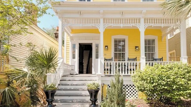 A yellow building with a white porch and steps leading to the entrance.