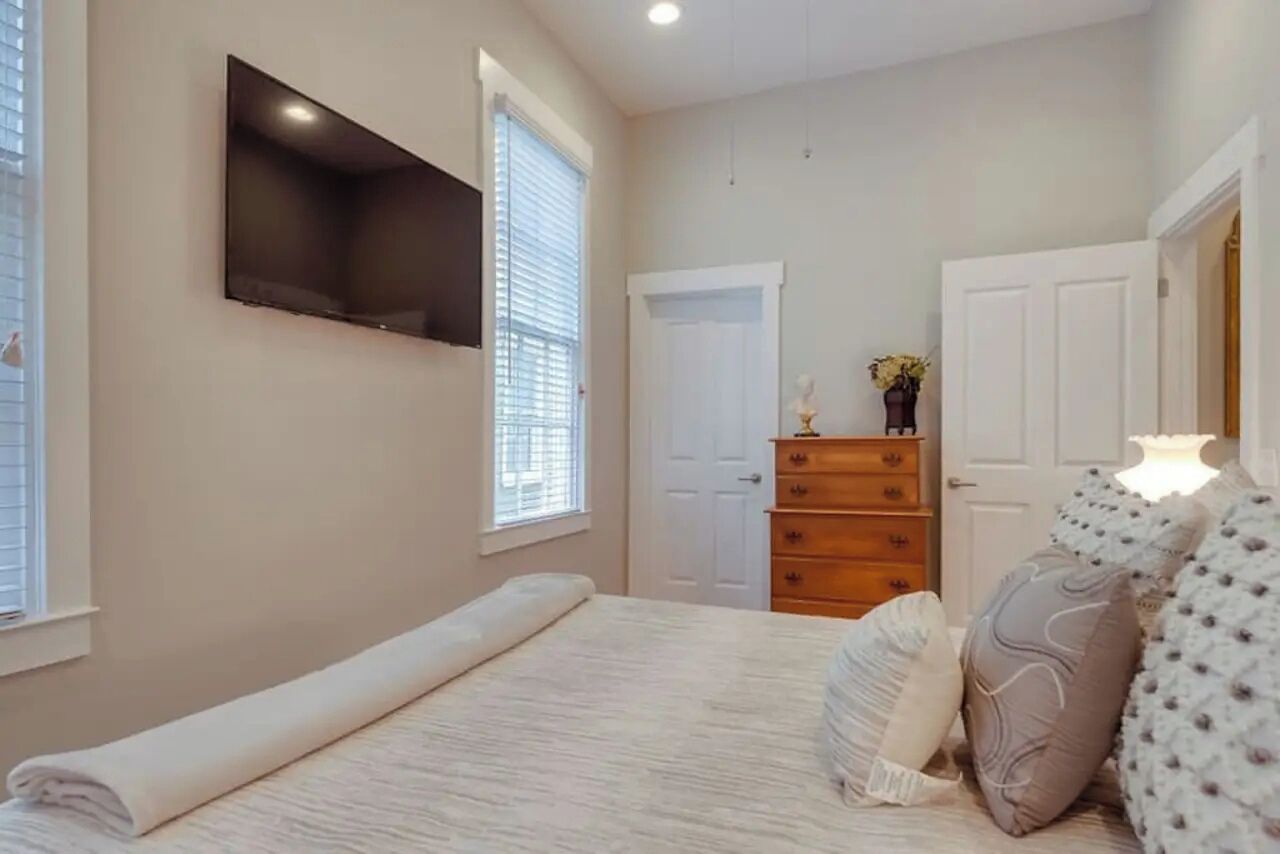 A bedroom with a bed, a dresser, a television mounted on the wall, and a door.