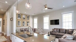 A modern kitchen with a central island, pendant lighting, a ceiling fan, and a dining area with patterned chairs.
