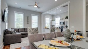 A modern living room with a gray sofa, a dining table with a decorative centerpiece, and a kitchen in the background.