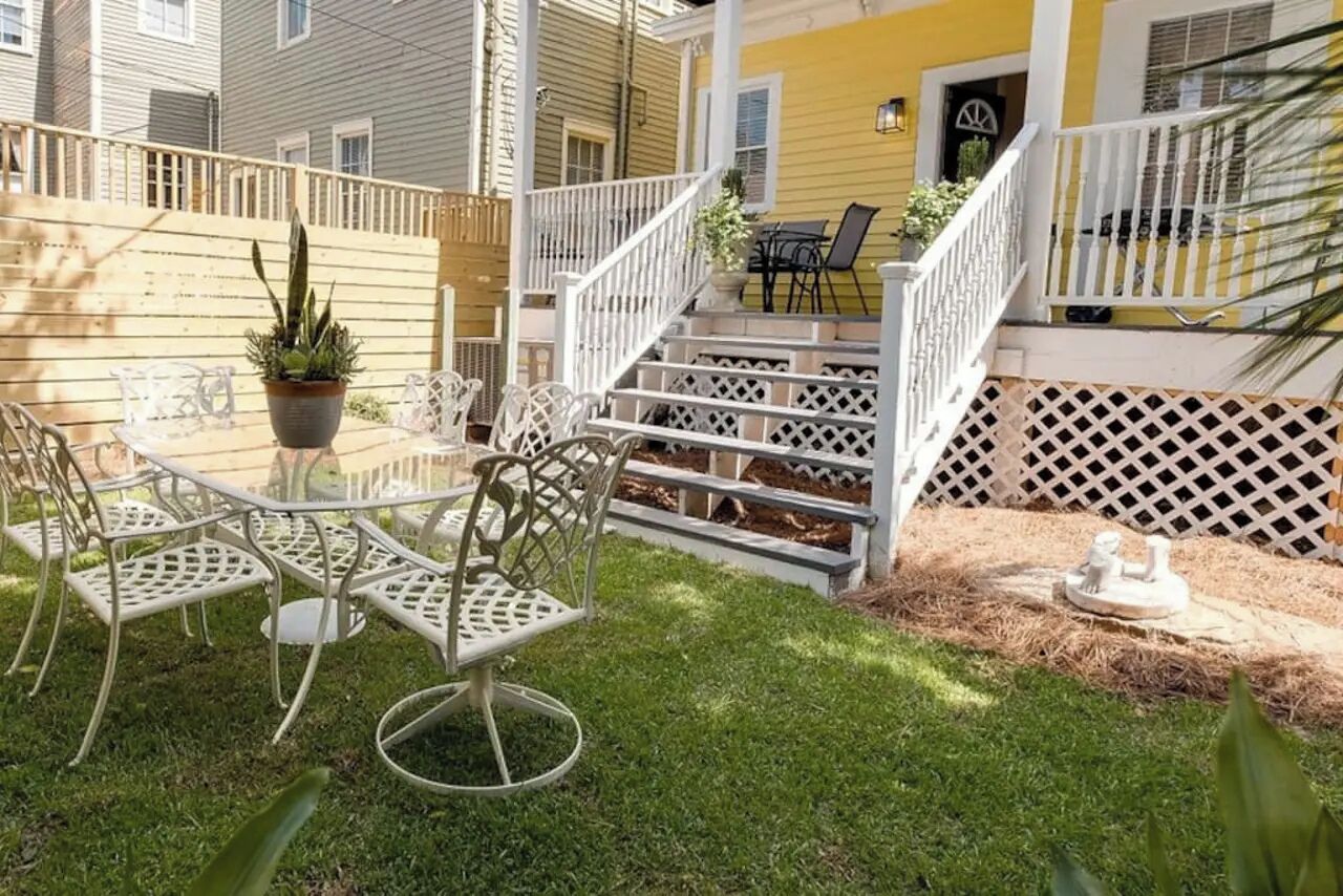 Un patio con mobiliario exterior, una escalera y un pequeño jardín.