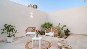 Eine Terrasse mit zwei Korbstühlen, einem kleinen Tisch, einem Blumentopf und einem Kaktus.