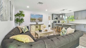 A modern living room with a grey sofa, a coffee table, and a dining area with a kitchen in the background. - Tropical Oasis •Pet-Friendly + Pool Clearwater (Largo)