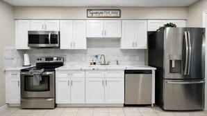 A modern kitchen with white cabinets, stainless steel appliances, a marble backsplash, and a sign above the cabinets. - Sleeps 8  • w Parking  • Fern Valley Retreat (Houston)