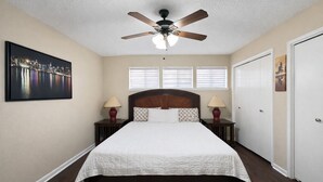A bedroom with a bed, two bedside tables, a ceiling fan, and two windows. - Sleeps 8  • w Parking  • Fern Valley Retreat (Houston)