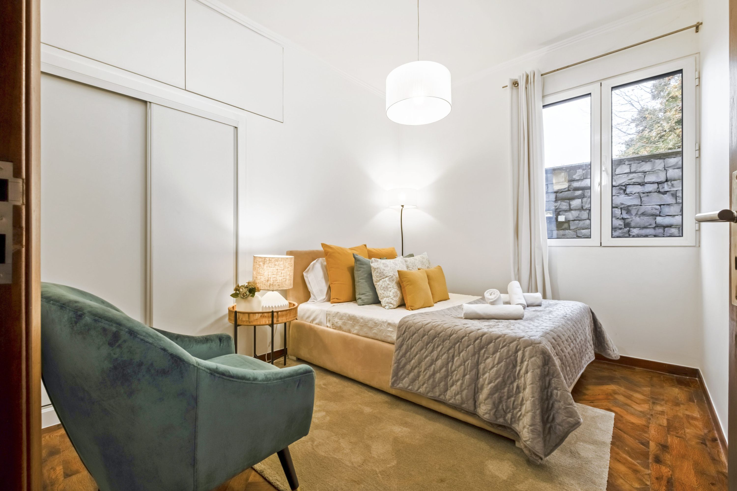 A bedroom with a bed, bedside table, lamp, and a chair.