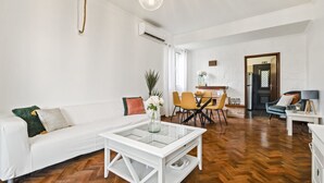 Un salon moderne avec un canapé blanc, une table basse en verre et un coin repas avec des chaises jaunes.