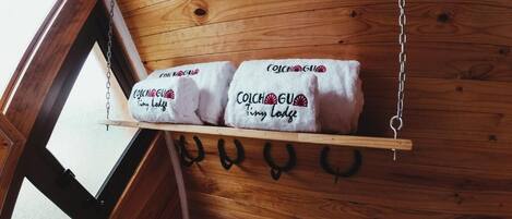 A wooden shelf with towels hanging on hooks, labeled "Colchagui Tiny Lodge."