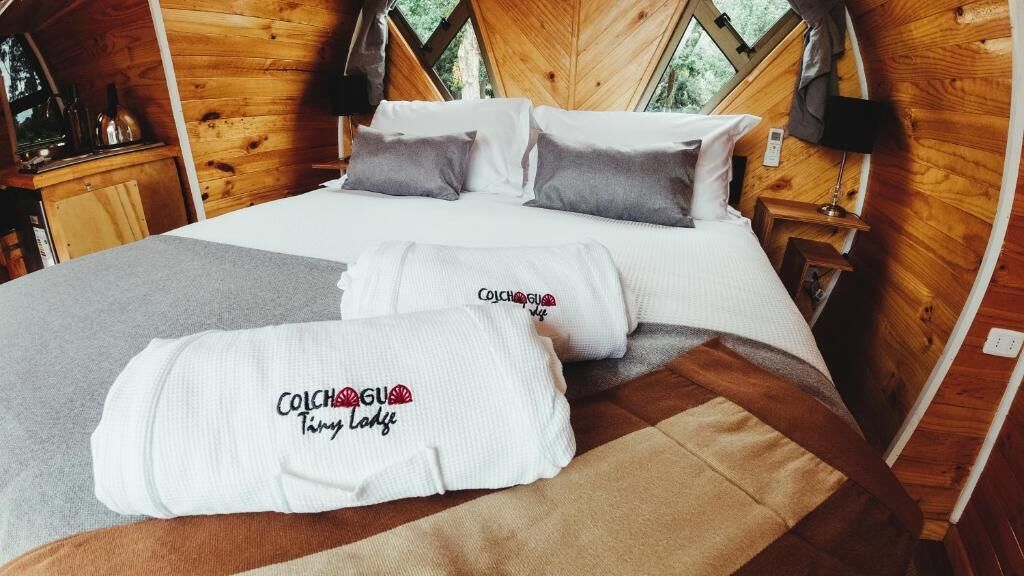Un dormitorio rústico con cabaña de madera, cama, almohadas y mesita de noche.