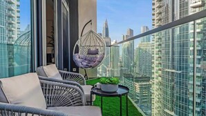 A balcony with wicker furniture, a hanging chair, and a small table with a plant. - Luxurious 3BR, Full Burj Khalifa & Fountain view (Dubai)
