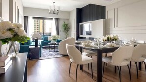 A modern dining area with a dark wood table, white chairs, and a large flat-screen TV mounted on the wall. - Luxurious 3BR, Full Burj Khalifa & Fountain view (Dubai)