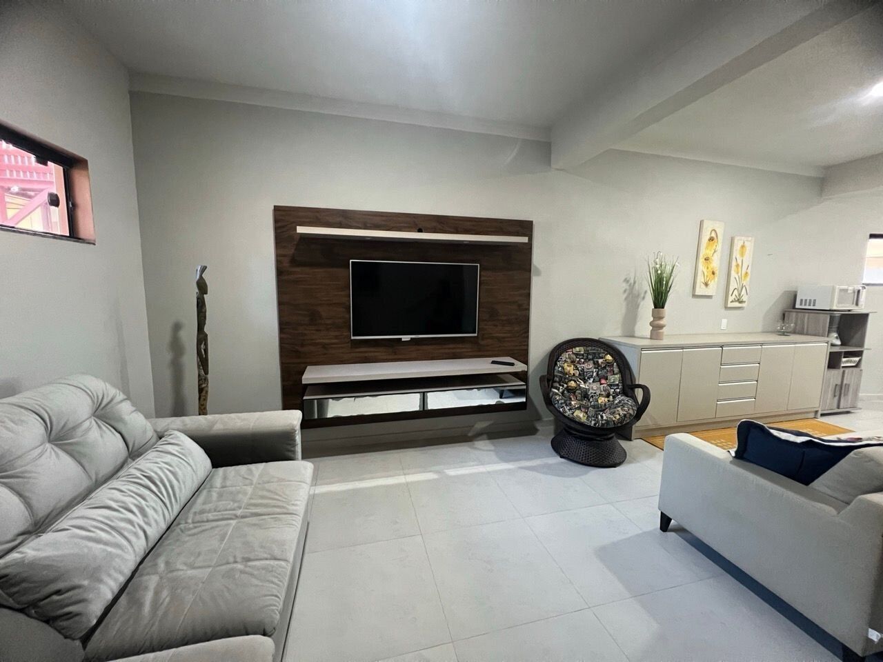 A modern living room with a flat-screen TV mounted on a wooden panel, two sofas, a coffee table, and a decorative chair.