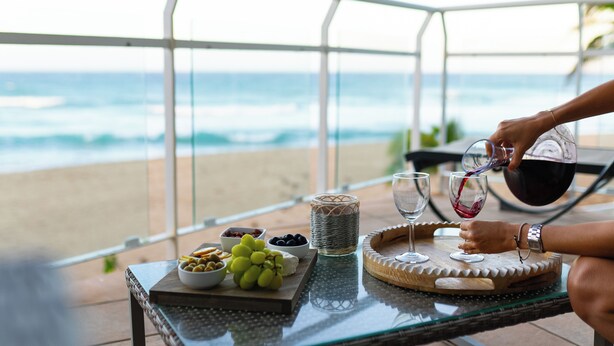 A table with snacks and wine glasses on a balcony overlooking the beach. - VILLA CUQUI – Stunning Ocean Views & Poolside Paradise at Sandy Beach, Rincon (Rincon)