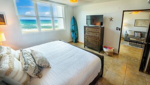A bedroom with a large bed, a TV, a surfboard, and a view of the ocean. - VILLA CUQUI – Stunning Ocean Views & Poolside Paradise at Sandy Beach, Rincon (Rincon)