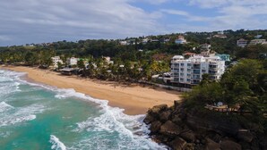 A coastal hotel with multiple floors, beachfront location, and a rocky shoreline. - VILLA CUQUI – Stunning Ocean Views & Poolside Paradise at Sandy Beach, Rincon (Rincon)