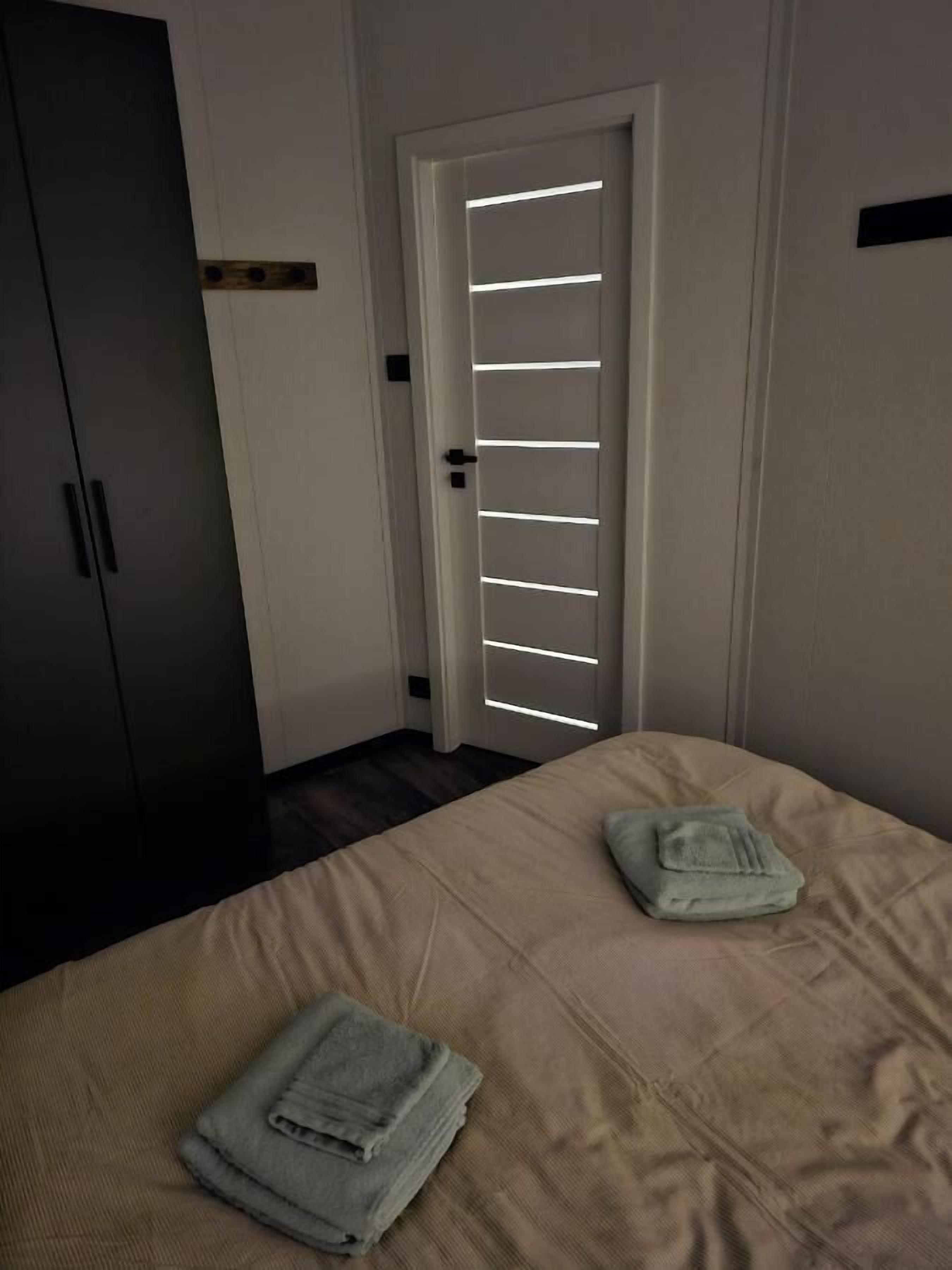 A bedroom with a bed, a wardrobe, and a door with horizontal light strips.