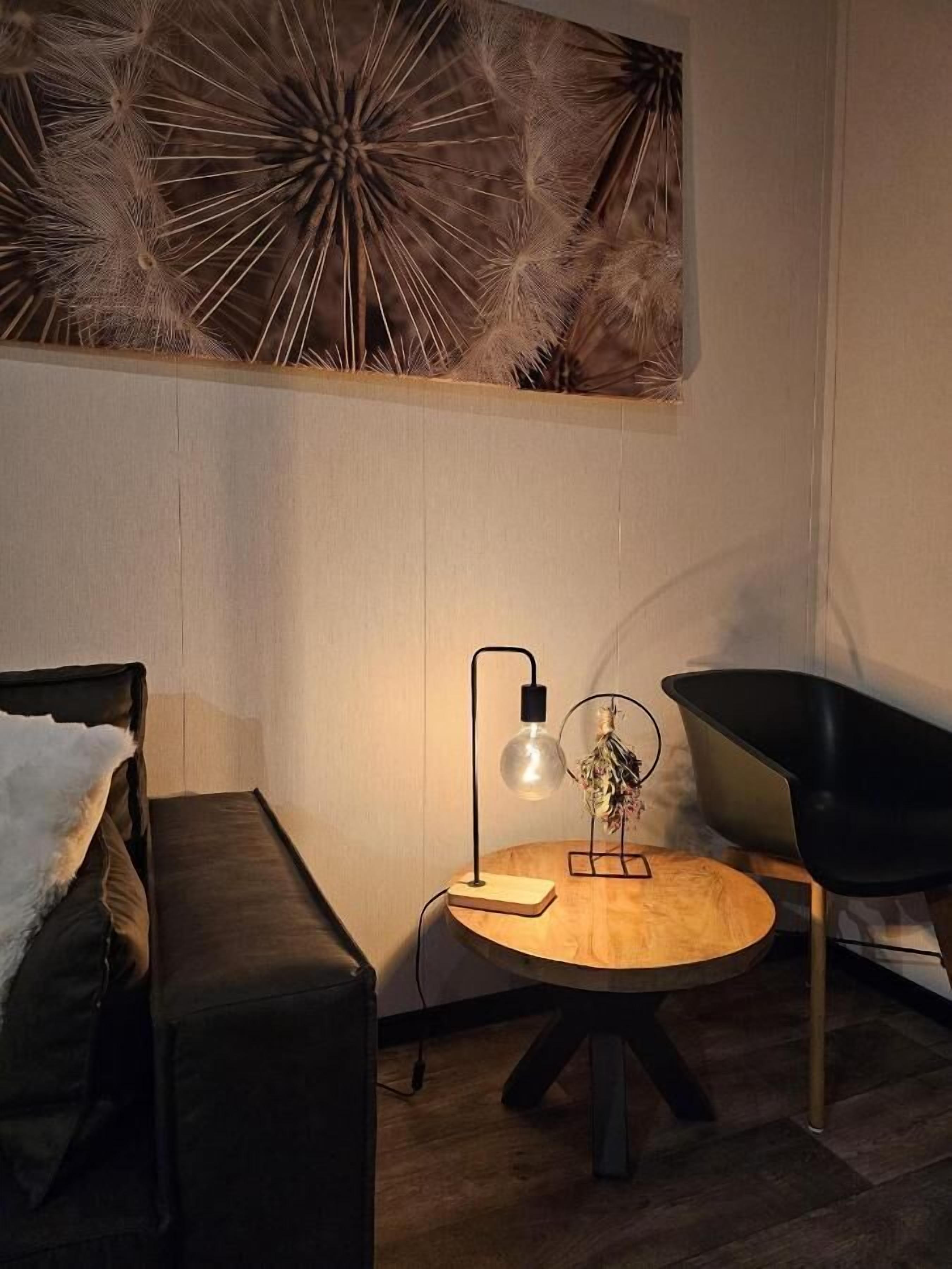 A cozy room with a round wooden table, a modern lamp, a black chair, and a decorative wall piece.