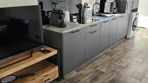 Moderni keittiö, jossa on harmaat kaapit, sisäänrakennettu uuni, kahvinkeitin ja pyykinpesukone.