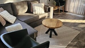Moderni olohuone, jossa on nahkasohva, musta nojatuoli, puinen sohvapöytä ja ruokailutila, jossa on tuoli ja lamppu.