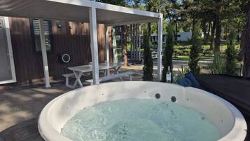 Ein Whirlpool in einem überdachten Außenbereich mit Holzterrasse und Picknicktisch.