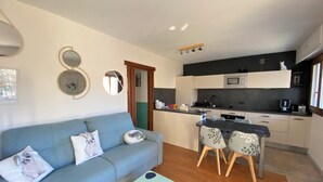 A modern living room with a sofa, a dining table with chairs, a kitchen area, and a small island with a microwave and sink. - 06CO : beautiful apartment at the foot of the slopes with balcony (Guillaumes)
