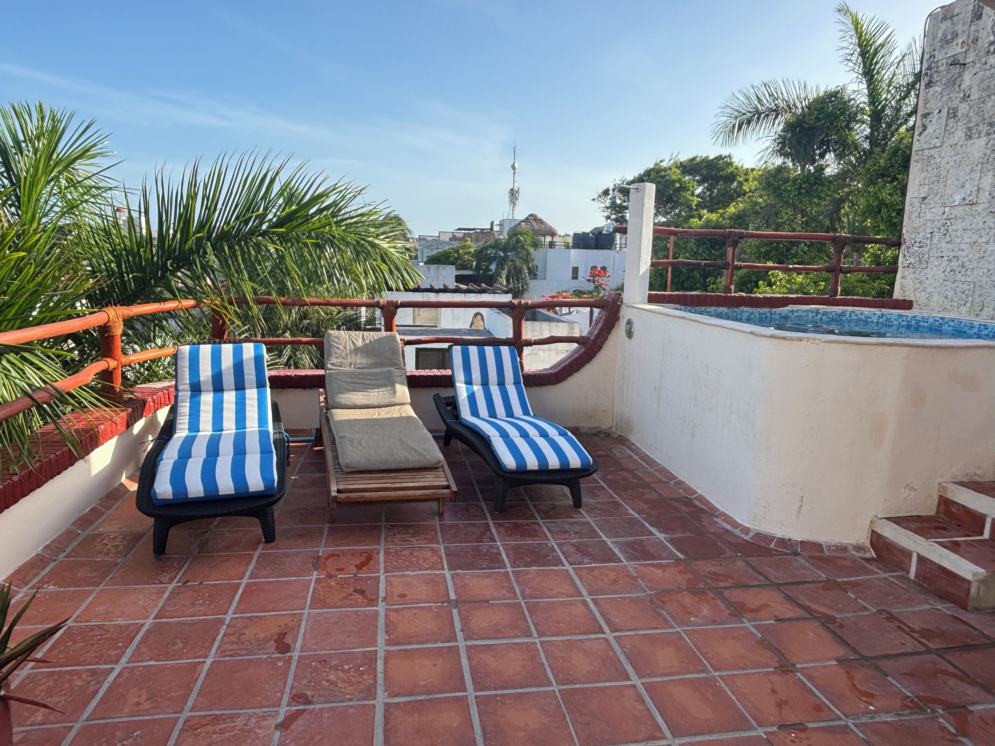 A rooftop terrace with two striped lounge chairs, a small table, and a view of the cityscape.