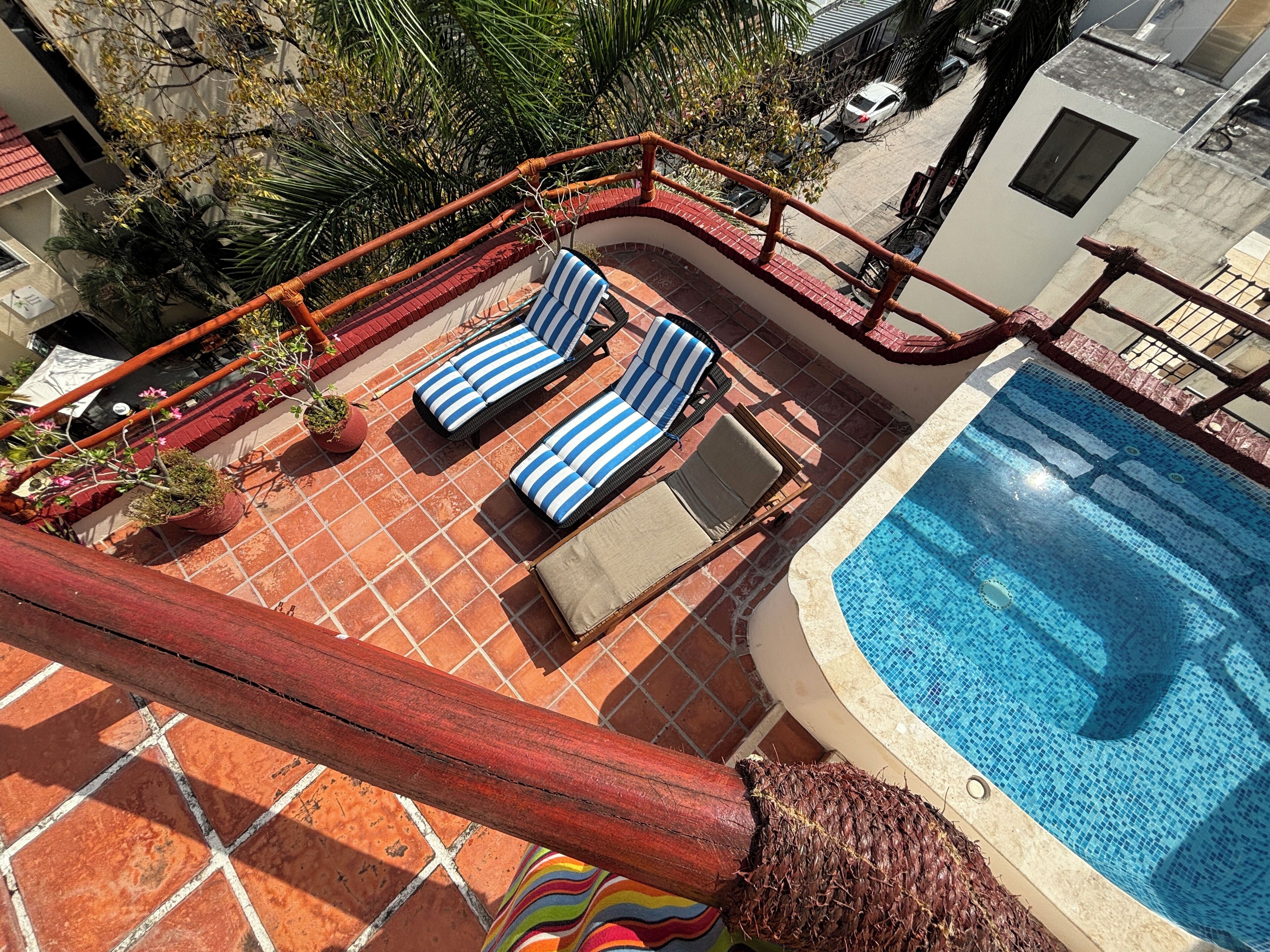 Ein Poolbereich auf dem Dach mit zwei Liegestühlen, einem Pool und einer roten Brüstung.