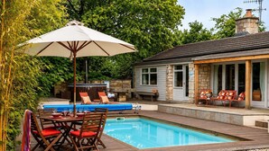 Un área de piscina con mesa y sillas, un conjunto de sillones de descanso y una zona de estar cubierta.