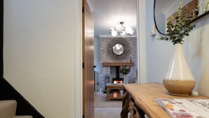 Ein Flur, der in einen Wohnbereich mit Kamin, Spiegel und einer Vase auf einem Tisch führt.