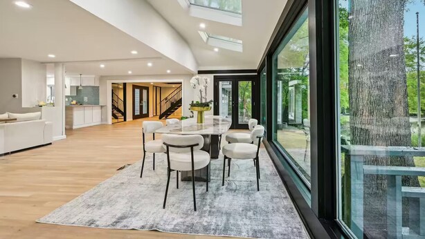 A spacious modern kitchen with a central island, a dining area with a round table and chairs, and a large window offering a view of the outdoors.