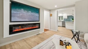 A modern living room with a large flat-screen TV, a fireplace, and a glass coffee table.