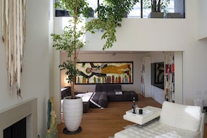 Una sala de estar moderna con un sofá seccional, un sofá blanco, un gran árbol en maceta y un cuadro abstracto colorido en la pared.