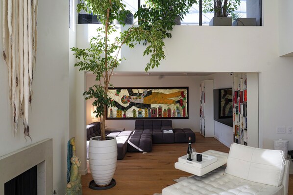 Una sala de estar moderna con un sofá seccional, un sofá blanco, un gran árbol en maceta y un cuadro abstracto colorido en la pared.