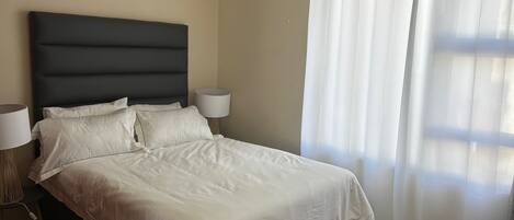 A neatly made bed with white linens, a dark headboard, and two bedside lamps.
