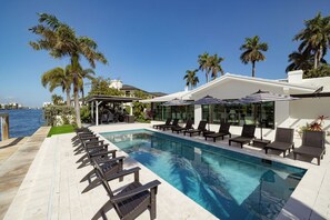 A pool area with lounge chairs, palm trees, and a view of the ocean.