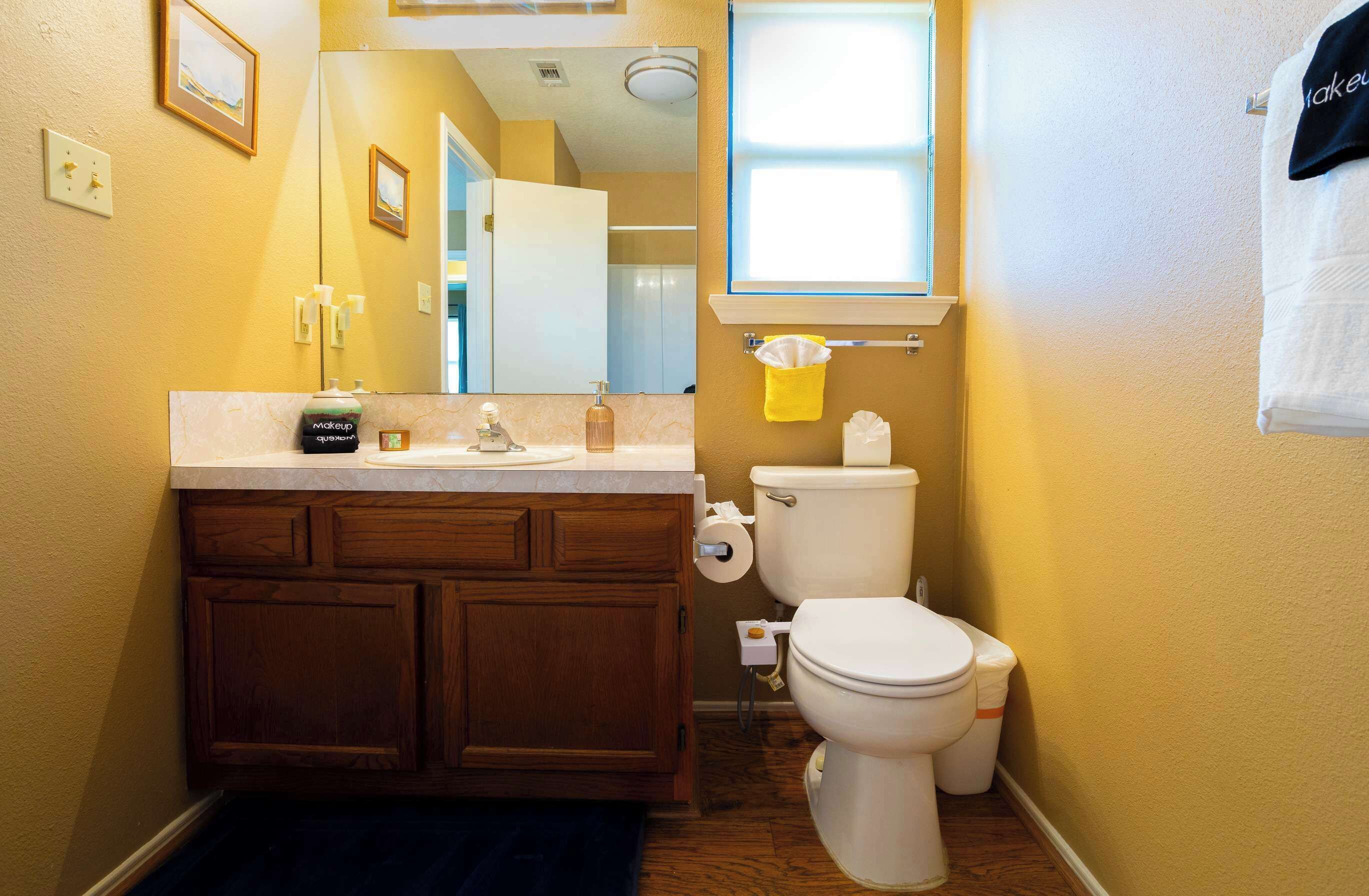 A bathroom with a wooden vanity, a toilet, a mirror, and a window.
