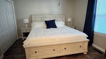 Une chambre à coucher avec un grand lit, un ventilateur de plafond, une table de chevet avec une lampe et une fenêtre avec des rideaux.