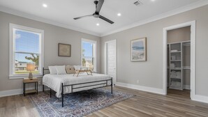 A bedroom with a bed, a ceiling fan, a window, a nightstand, and a walk-in closet.