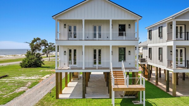 A two-story waterfront house with a balcony on the upper floor, a covered outdoor area, and a view of the ocean.