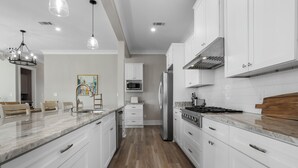 A modern kitchen with white cabinetry, a marble countertop, stainless steel appliances, and pendant lighting.