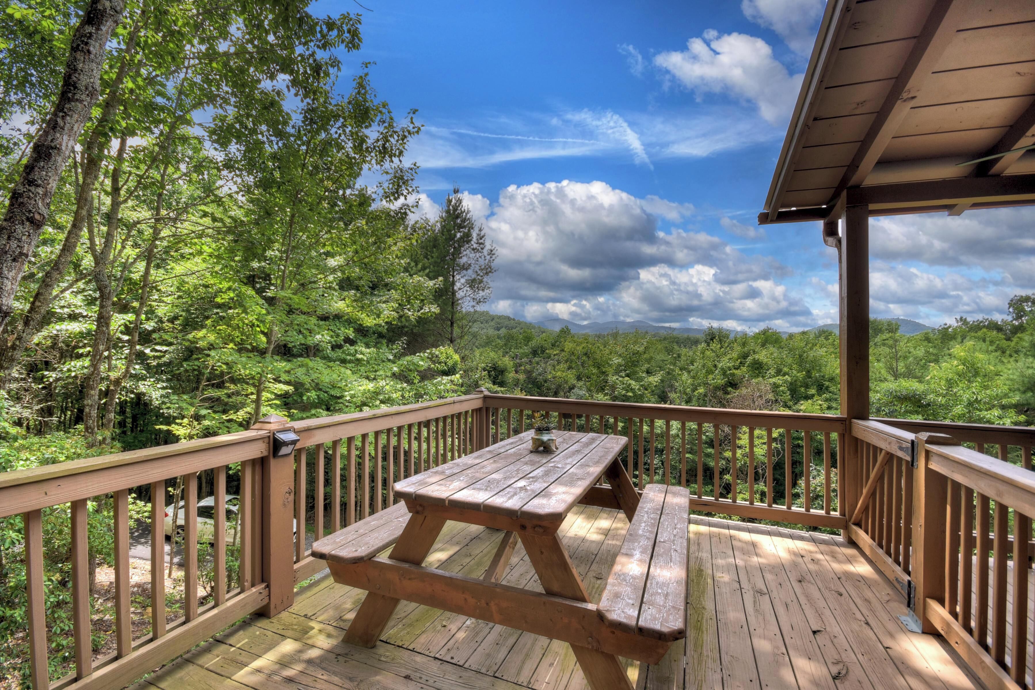 A wooden deck with a picnic table and benches, surrounded by lush greenery and trees.