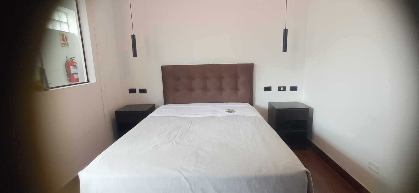 Une chambre d’hôtel avec un lit simple, deux tables de chevet, une tête de lit et un extincteur fixé au mur.