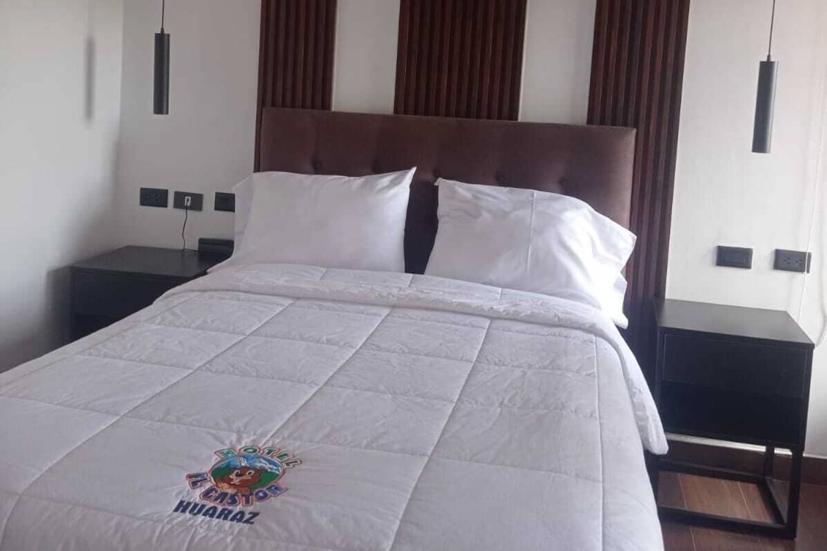 A hotel room with a large bed, wooden headboard, two bedside tables, and pendant lights.