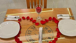 A dining table with a heart-shaped arrangement of rose petals, a glass of red wine, and a small vase with a red rose. - HOTEL EL CASTOR UCHUYACU HUARAZ (Tarica)