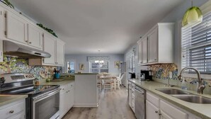 A kitchen with white cabinets, a central island, stainless steel appliances, and a window with blinds.