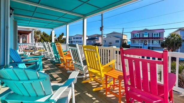 A covered porch with colorful Adirondack chairs and a view of houses in the background.